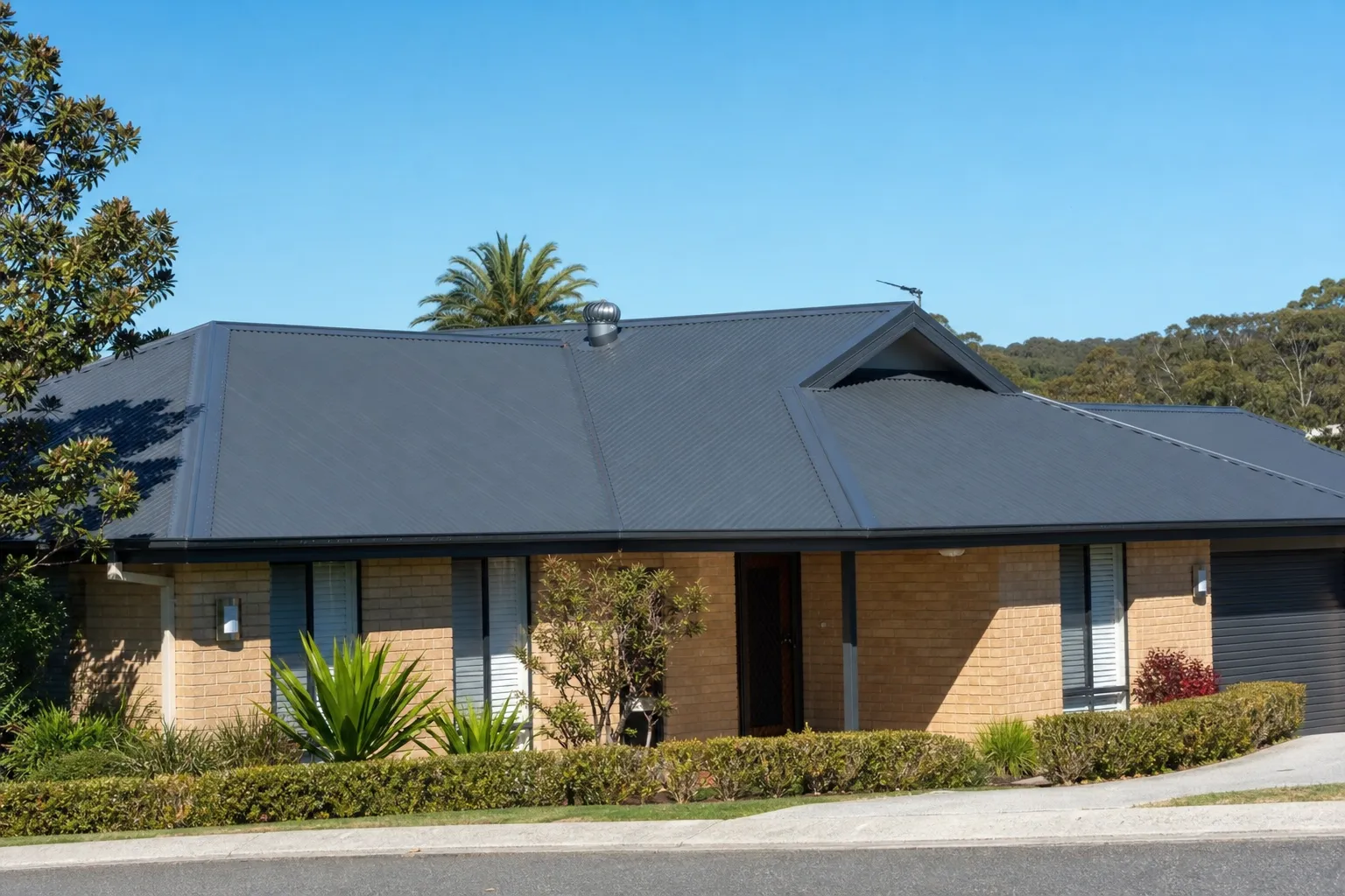 Central Coast home with a new dark grey Colorbond metal roof against a blue coastal sky