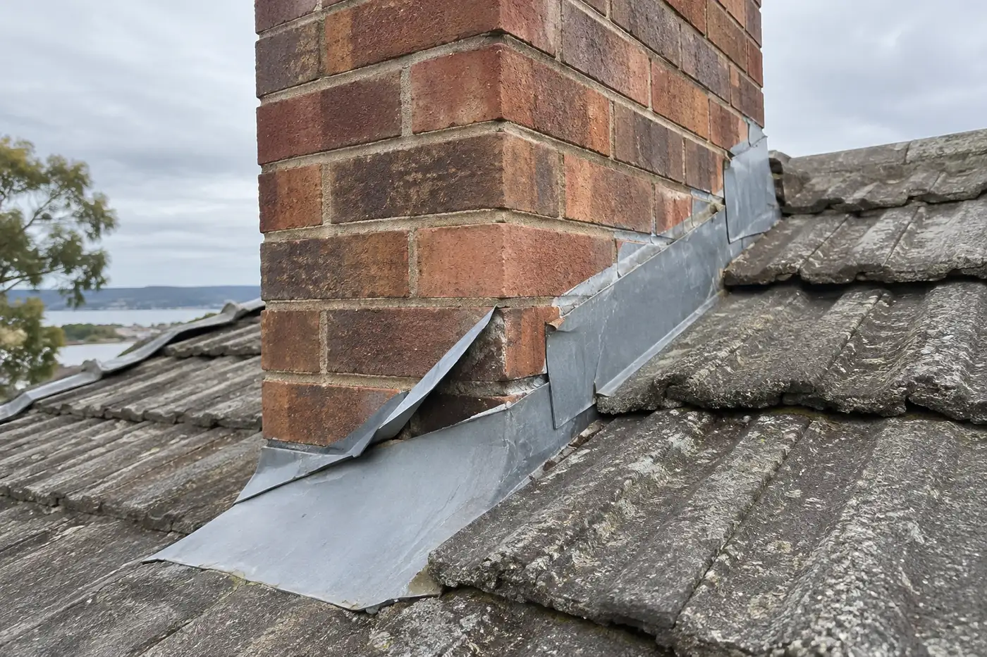 Metal flashing lifting away from a brick chimney on a concrete tile roof