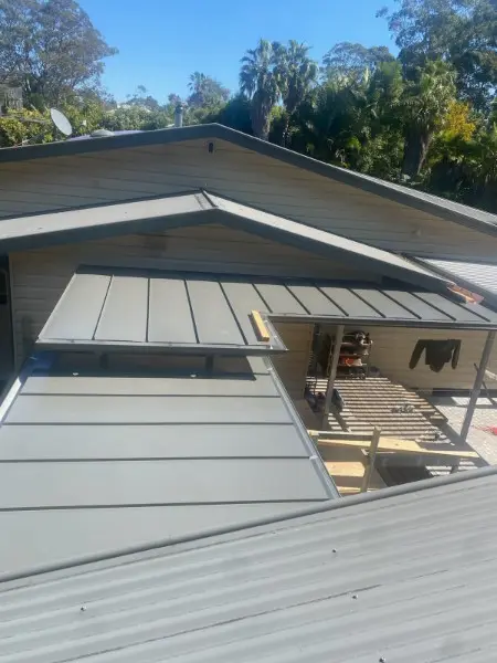 Flat pan metal roof going on over a covered outdoor area of a timber clad home