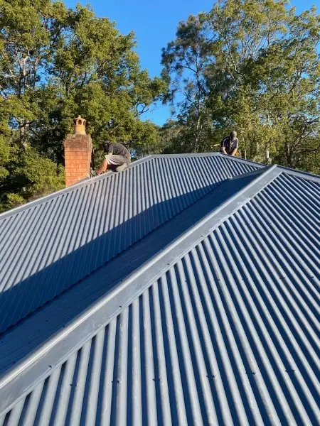 Our roofers working at the ridge of a new corrugated metal roof beside a brick chimney