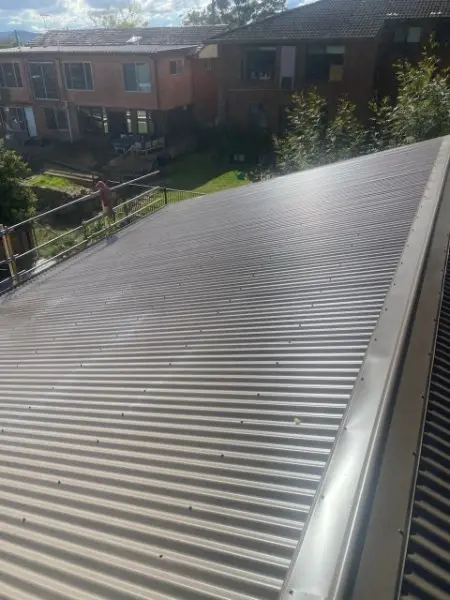 Dark grey metal roof with edge safety rail in place, beside brick units