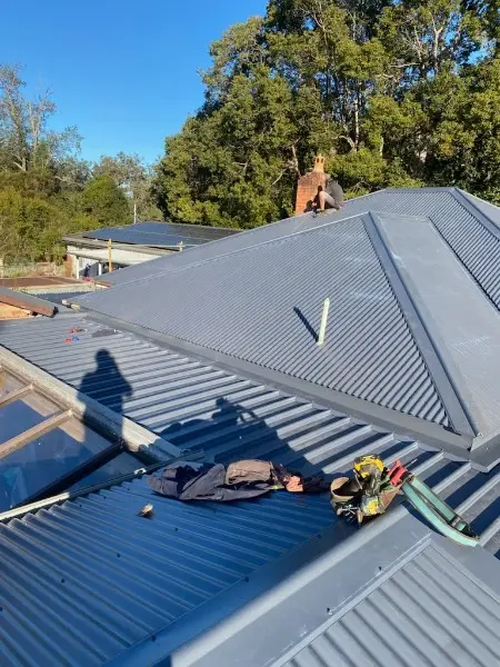 New grey metal hip roof with a vent pipe and the crew's tools laid out on the sheets