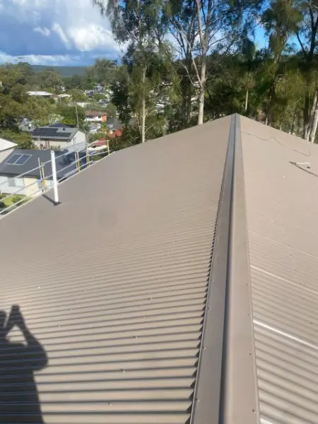 Brown metal roof ridge capping running toward a leafy valley view