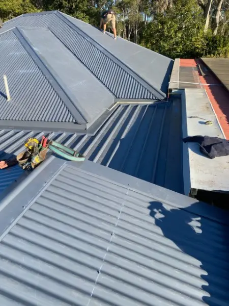 Grey metal re-roof with a long valley flashing and a roofer on the far ridge