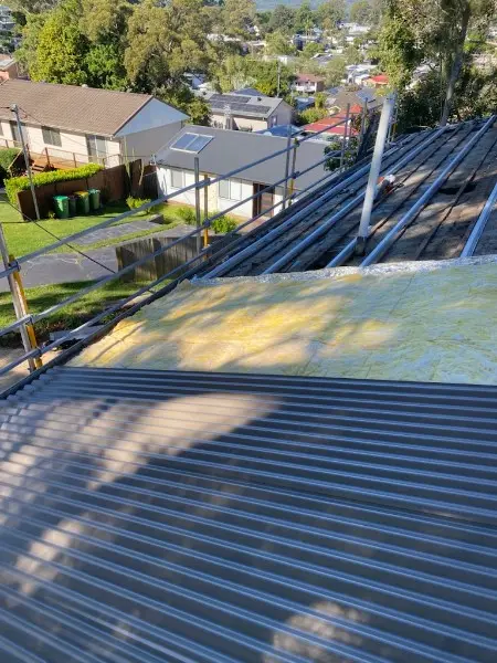 New metal sheets laid beside the old lichen covered roof during a re-sheet, with scaffold at the edge