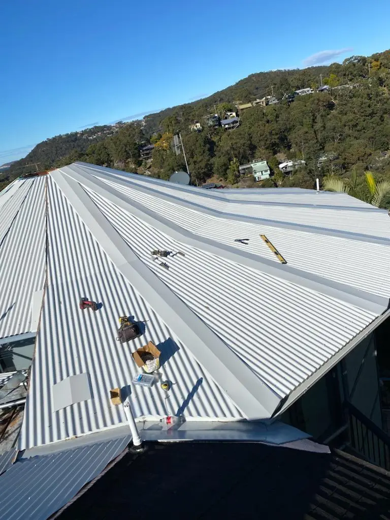 Tapered metal sheets being fixed on an octagonal roof overlooking bushland and water