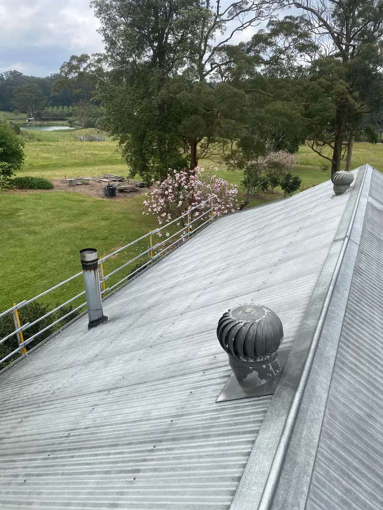 Weathered, streaky corrugated metal roof on an acreage home in Somersby, with a whirlybird vent and edge safety rail