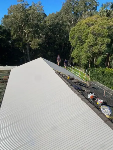 New pale metal sheets fixed along a roof while the old tiles are still being removed further along